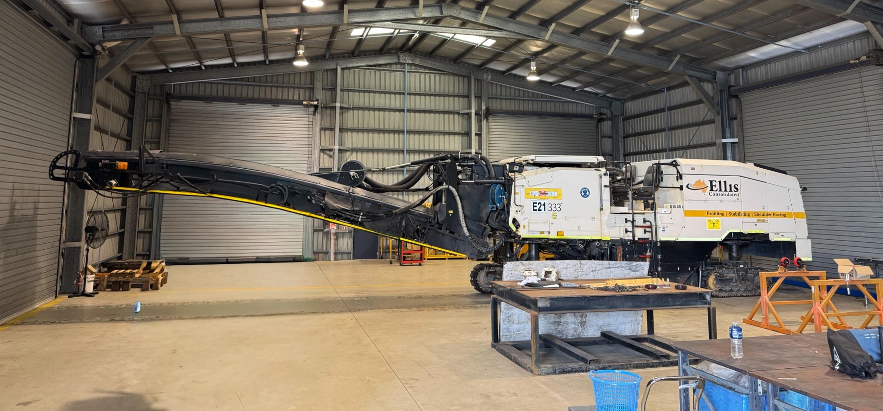 Road-profiling machine with its discharge conveyor extended inside a workshop.